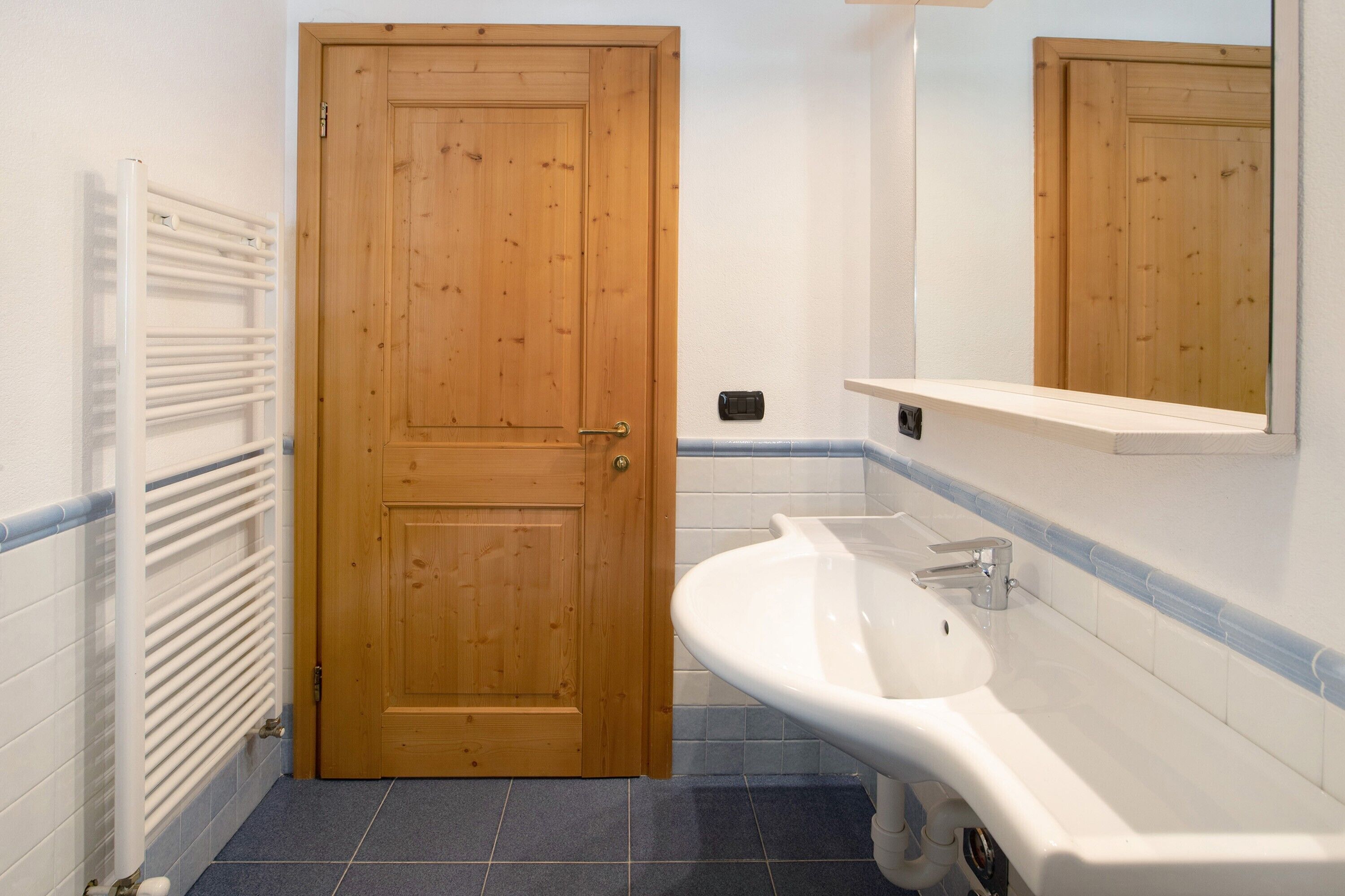 A bathroom with a wooden door, white sink, and blue-tiled floor.