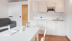 A compact kitchen with white cabinets, a microwave, and a sink. There's a dining table with a book and cups. - Apartment 'Baita Valandrea 3' with Mountain View, Shared Garden and Wi-Fi (Livigno)