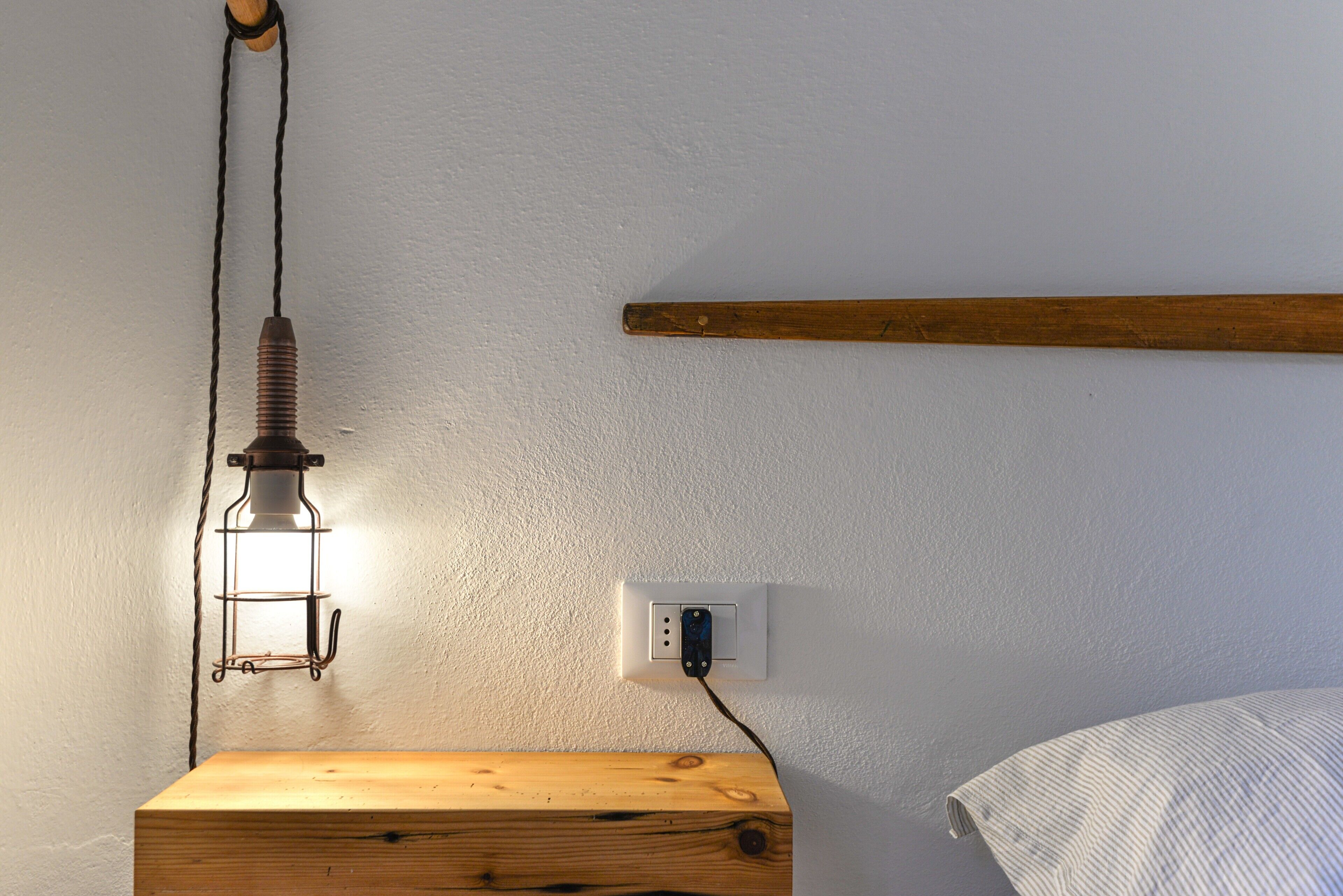 Ein Nachttisch aus Holz mit Lampe, Steckdose und einem Holz-Kopfteil vor einer weißen Wand.