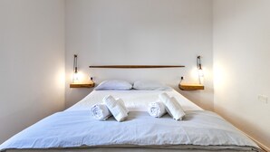 Et hotelværelse med en seng, to vægmonterede lamper og en træhylde over sengen.