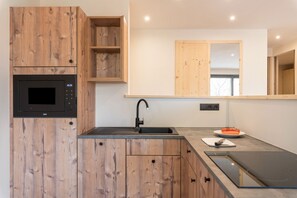 Une cuisine moderne avec des meubles en bois, un four à micro-ondes encastré, un évier et un plan de travail agrémenté d’une planche à découper et de légumes.