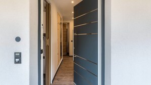 Een gang met een houten vloer, een deur met donker paneel en een lichtschakelaar aan de muur.