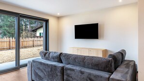 Una sala moderna con un sofá gris, un televisor montado y un mueble de madera.
