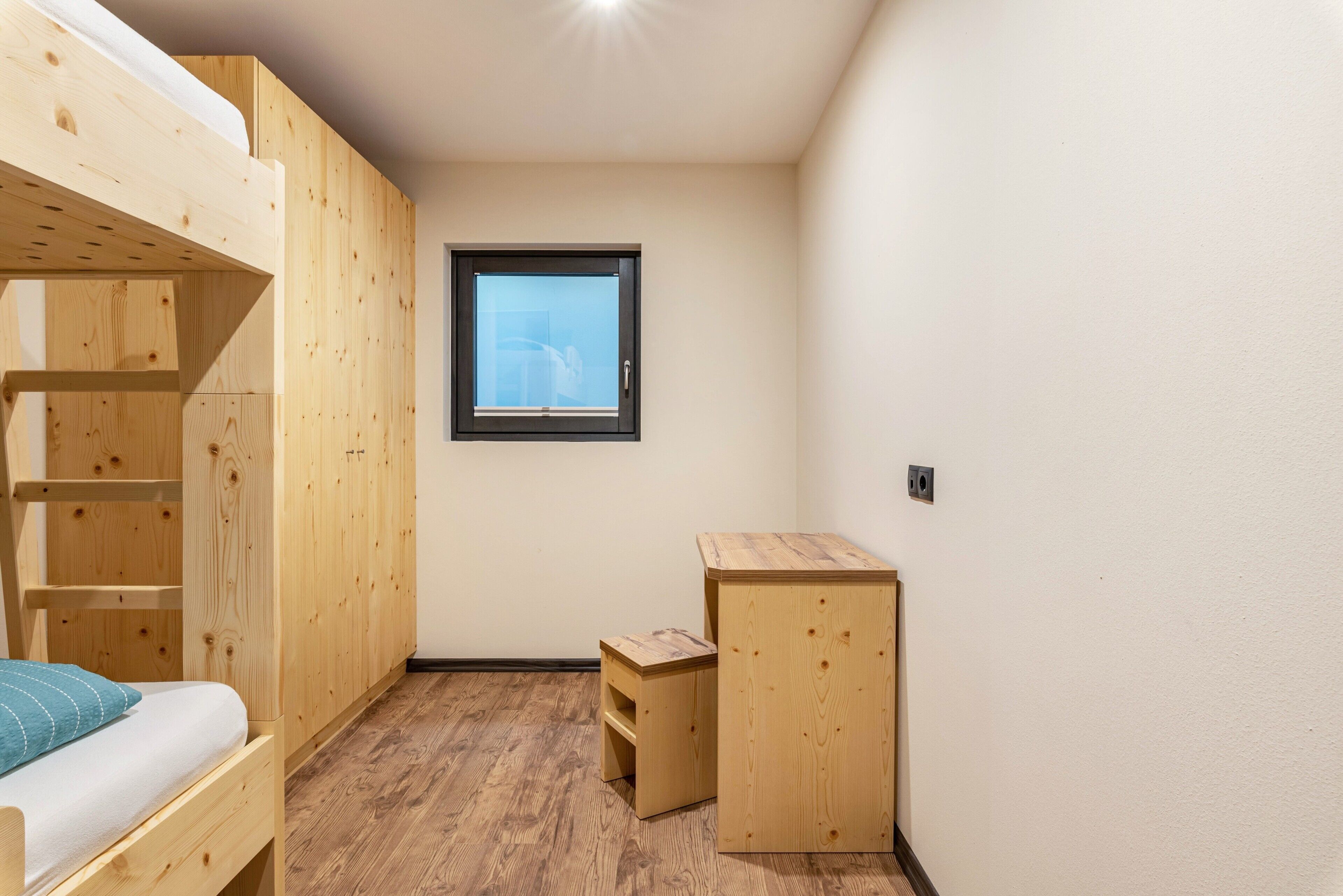 Una habitación con literas, un escritorio pequeño, una ventana y suelo de madera.