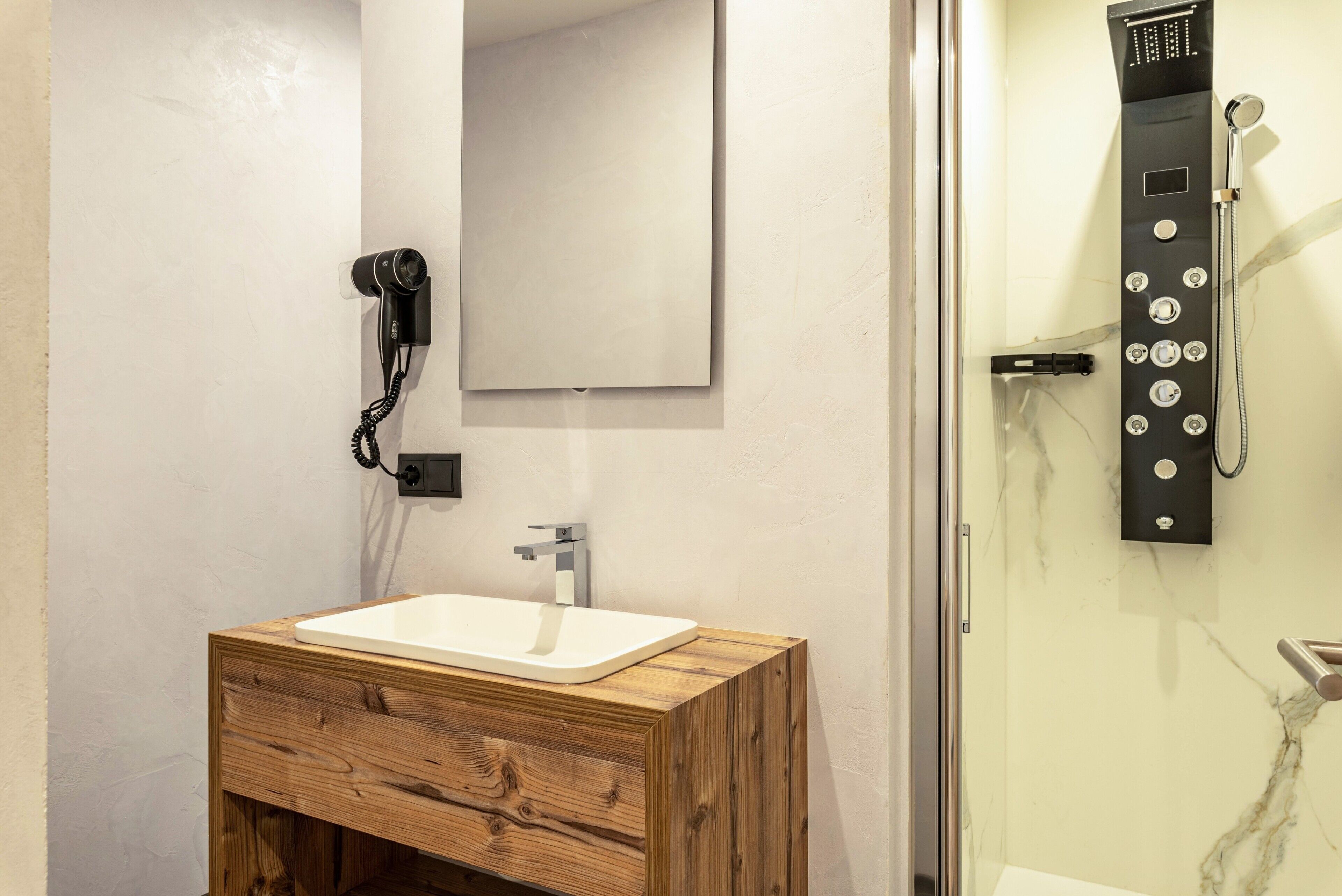 Un baño con tocador de madera, un espejo, un lavabo blanco, ducha con cabezal de mano y un teléfono.