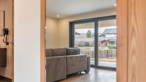 Un interior modern amb un sofà gris, terres de fusta i una gran porta corredissa de vidre que dona a una zona exterior.