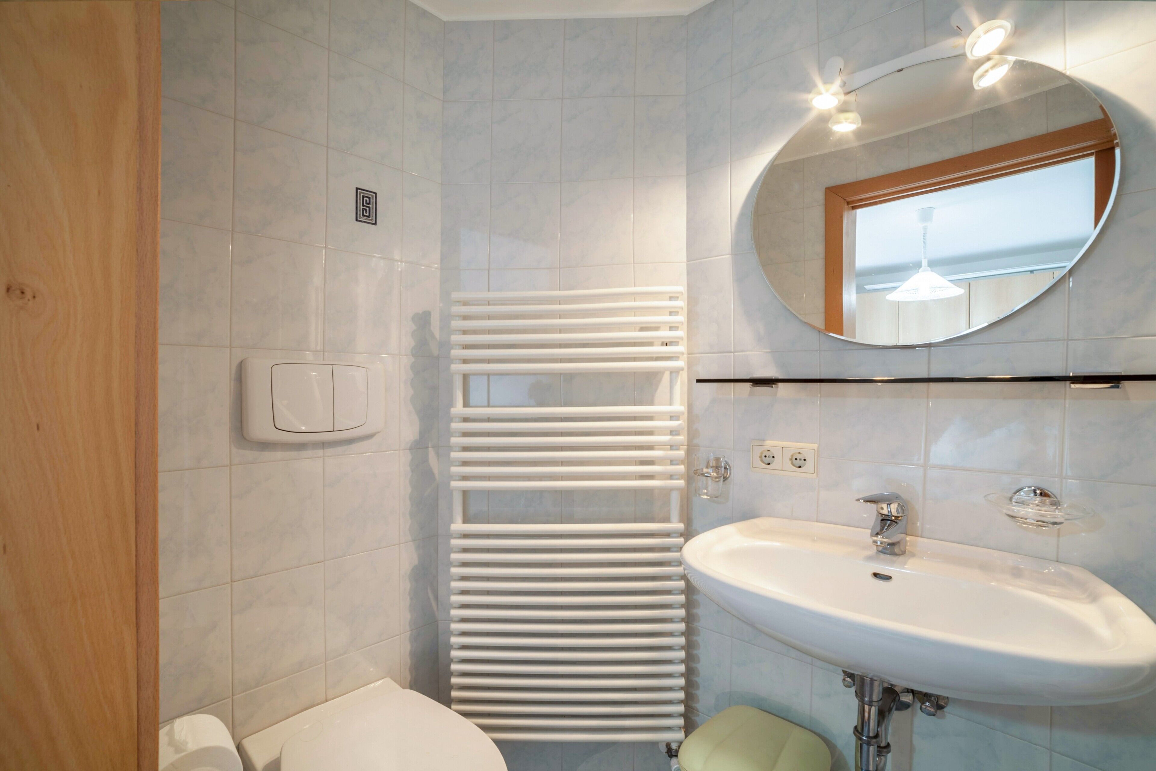 A bathroom with a white radiator, a sink, and a mirror.