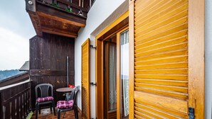 A balcony with a wooden railing, a table with two chairs, and a door with horizontal louvered shutters. - Farmhouse 'Bauernhof Oberkapillhof 2' with Mountain View, Shared Garden and Wi-Fi (Meltina)