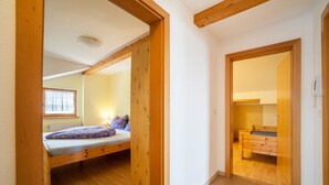 Una habitación con cama, vigas de madera, una ventana y una puerta que da a otra estancia.