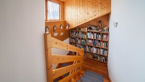 Una escalera de madera que lleva a un entrepiso con una estantería llena de libros y una pequeña repisa con objetos decorativos.