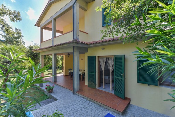 Une maison à deux étages avec un patio couvert, des volets verts et un jardin.