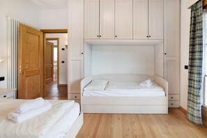 A bedroom with a bed, a wooden wardrobe, and a view of the hallway.
