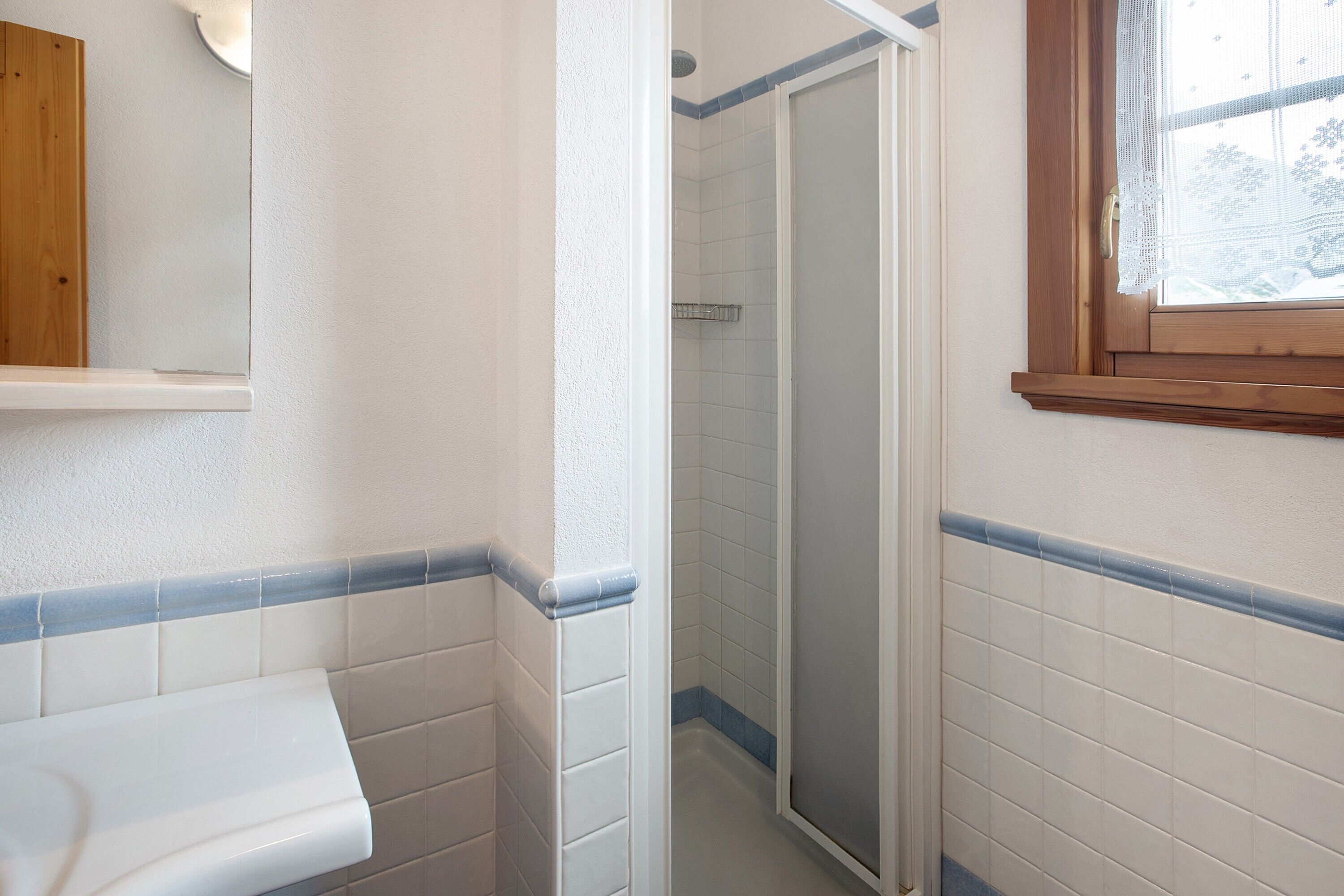 Une salle de bain avec des carreaux blancs, une étagère en bois et un espace douche.