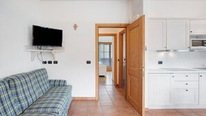 A living room with a sofa, a TV mounted on the wall, and a kitchen area with cabinets and a microwave. - Apartment 'Baita Valandrea 2' with Mountain View, Shared Garden and Wi-Fi (Livigno)