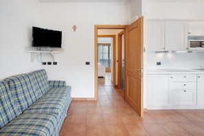 A living room with a sofa, a TV mounted on the wall, and a kitchen area with cabinets and a microwave.