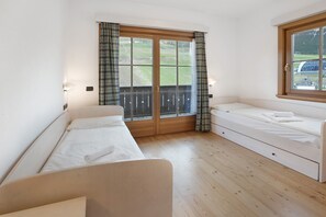 A room with two beds, a window with curtains, a wooden floor, and a view of a green landscape.