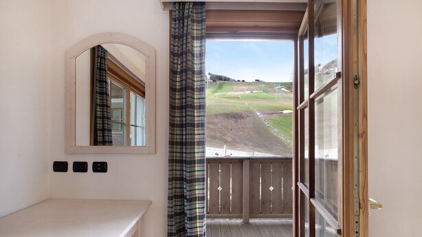 A room with a wooden bench, a small table, a mirror, and a view of a grassy area through a window. - Apartment 'Baita Valandrea 2' with Mountain View, Shared Garden and Wi-Fi (Livigno)