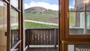 Un balcon en bois offrant une vue sur une colline verdoyante et un ciel dégagé.