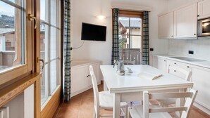 Une cuisine avec une table à manger, des chaises, un téléviseur et une fenêtre avec des rideaux.