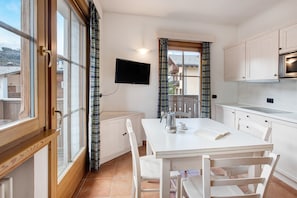 A kitchen with a dining table, chairs, a TV, and a window with curtains.