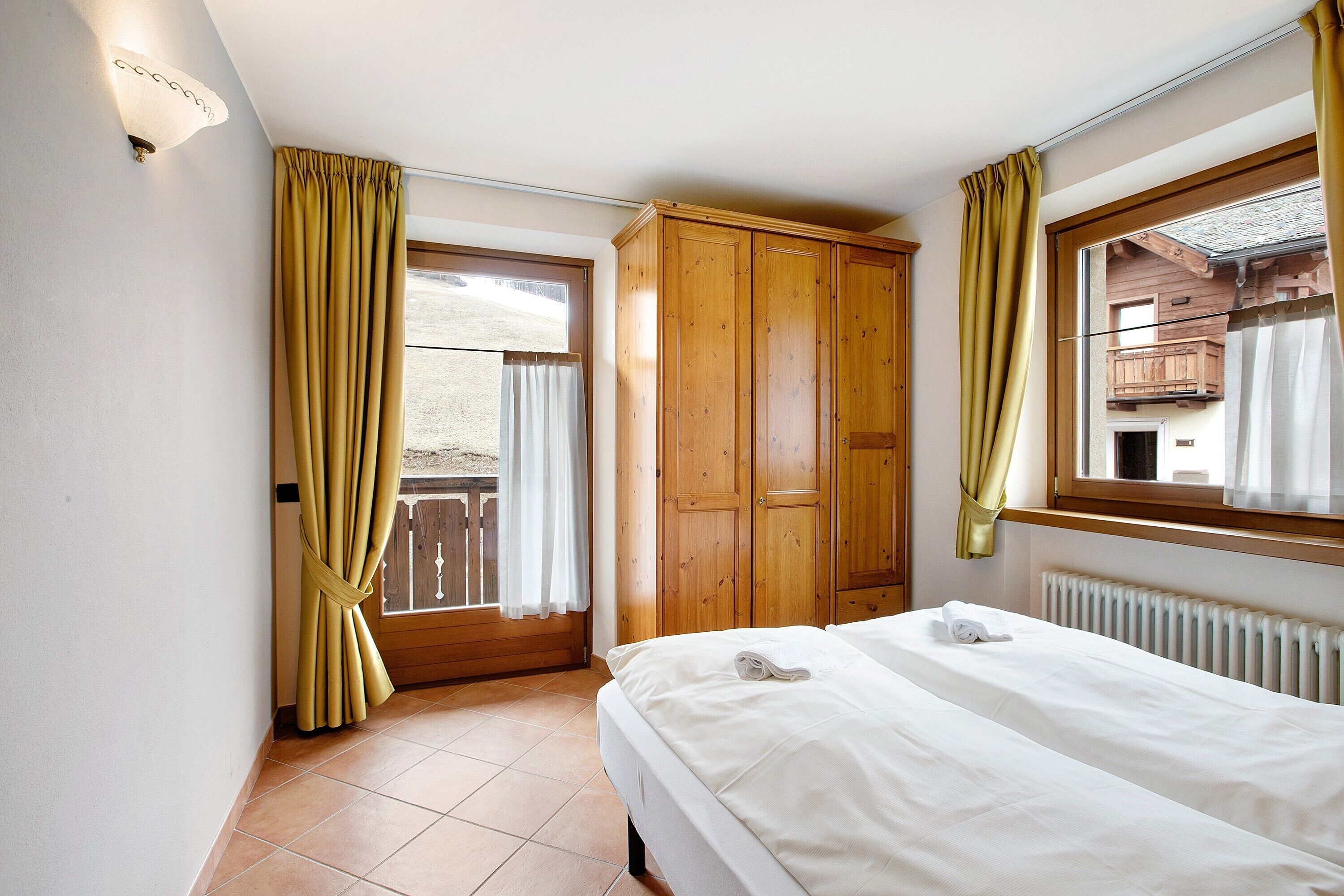 A bedroom with a bed, wooden wardrobe, and a window with curtains.