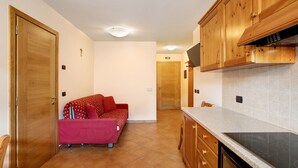 A kitchen with wooden cabinets, a countertop, and a red sofa in the living area. - Apartment 'Chalet Anna Cigambola' with Mountain View, Balcony and Wi-Fi (Livigno)