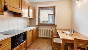 A kitchen with wooden cabinets, a built-in microwave, a window with curtains, and a dining table with chairs. - Apartment 'Chalet Anna Cigambola' with Mountain View, Balcony and Wi-Fi (Livigno)
