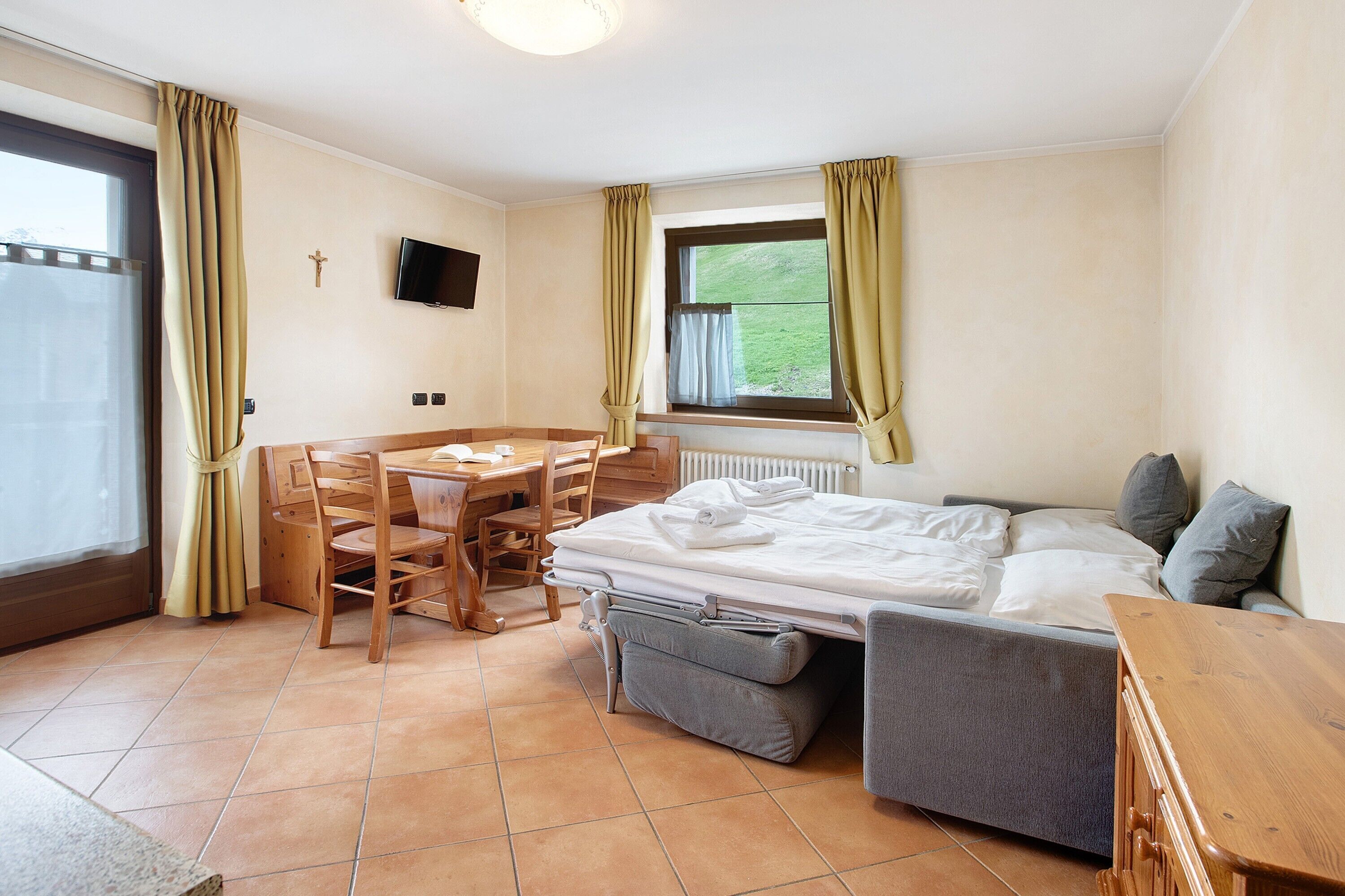 Ein Zimmer mit einem Bett, einem Schreibtisch, einem Stuhl, einem Fernseher und einem Fenster mit Vorhängen.