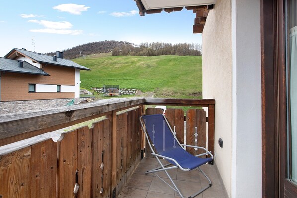 A balcony with a wooden fence, a blue lounge chair, and a view of a green hillside.