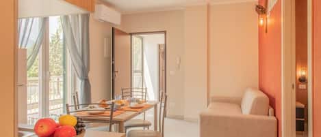 A dining area with a table set for two, a bowl of fruit, and a sofa in the adjacent living area.
