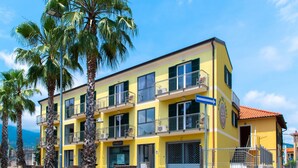Un edificio giallo a più piani con balconi, palme e un cielo azzurro limpido.