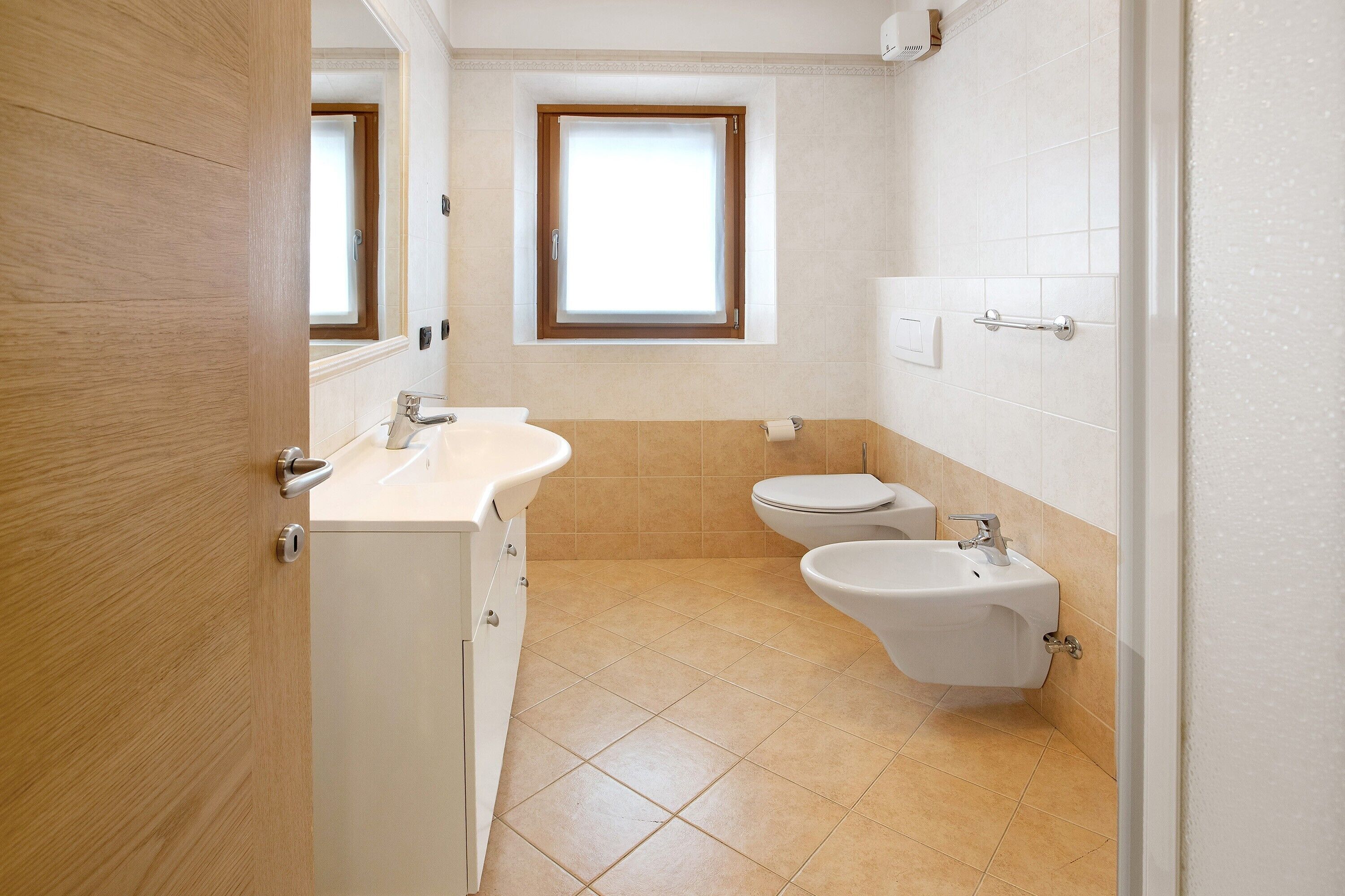 Een badkamer met toilet, bidet en wastafel, een raam en een houten deur.