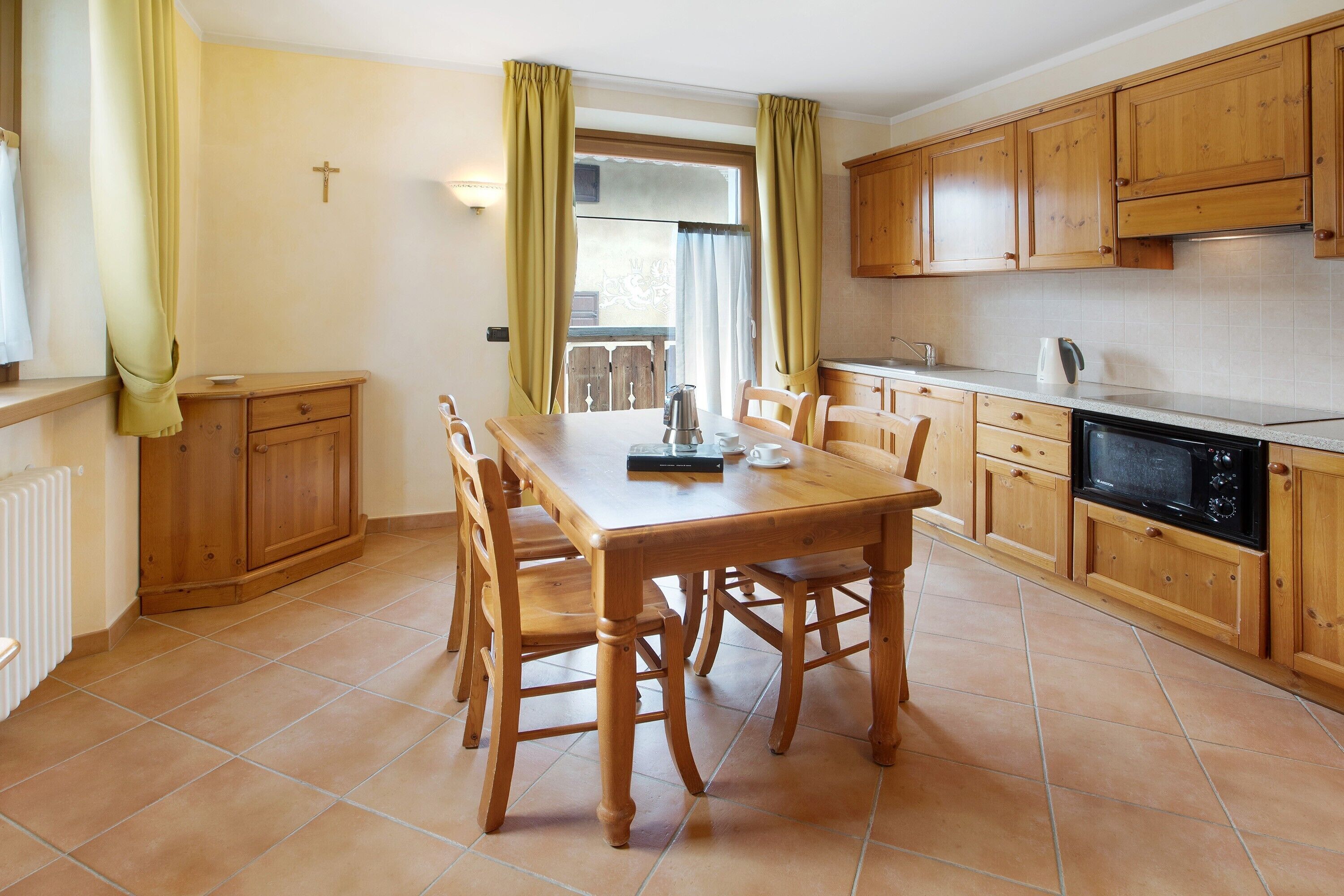 A kitchen with wooden cabinets, a dining table with chairs, a window with curtains, and a radiator.