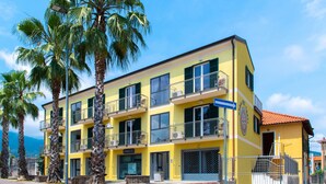 Un immeuble jaune à plusieurs étages, doté de balcons, de palmiers et surplombant un ciel dégagé.