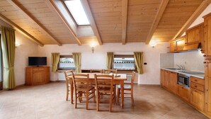 Eine geräumige Küche mit Holzausbau, einem Esstisch mit Stühlen, einem Fernseher und einem Oberlicht.