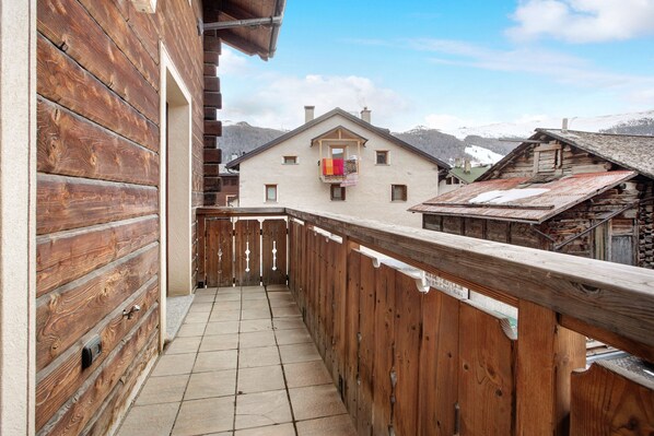 Un balcon en bois doté d’un sol carrelé, d’une balustrade en bois et offrant une vue sur une montagne.