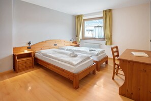 Une pièce comprenant deux lits en bois, un bureau en bois, une chaise, une table de chevet et une fenêtre avec des rideaux.
