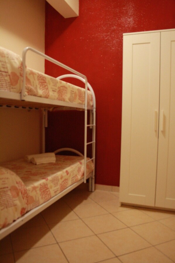 A bunk bed with a patterned bedspread, a white wardrobe, and a red wall.