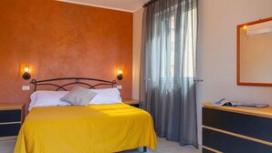 Een slaapkamer met een bed, twee bedlampen, een raam met gordijnen en een bureau met een stoel.