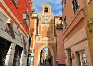 Una calle estrecha con una imponente torre del reloj, un paseo peatonal y edificios de arquitectura tradicional.