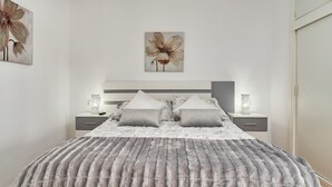 Ein Schlafzimmer mit einem Bett, zwei Nachttischen, einem Wandbild und einer flauschigen, grauen Decke.