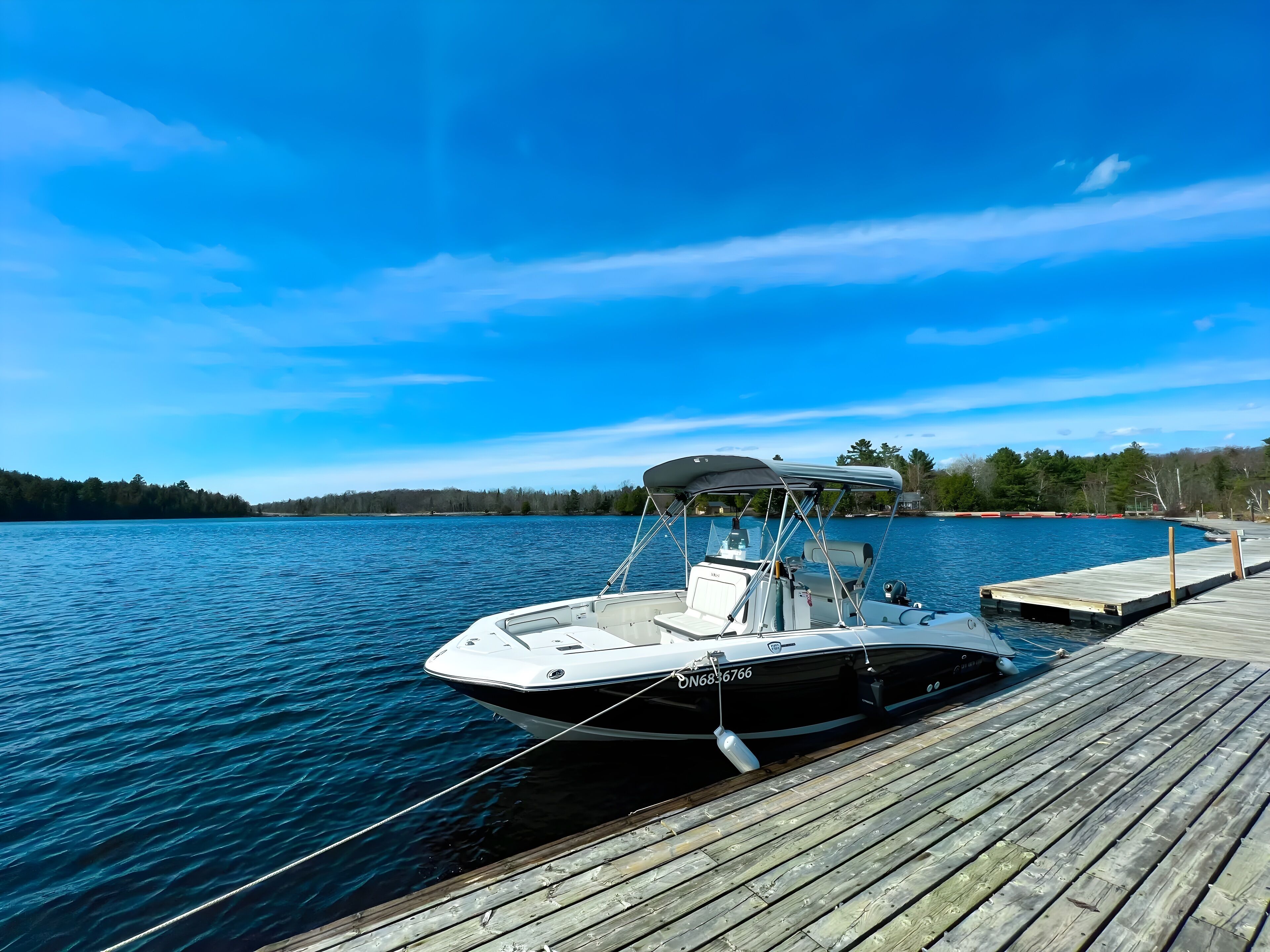 A boat docked at a wooden pier with calm water and a clear sky.