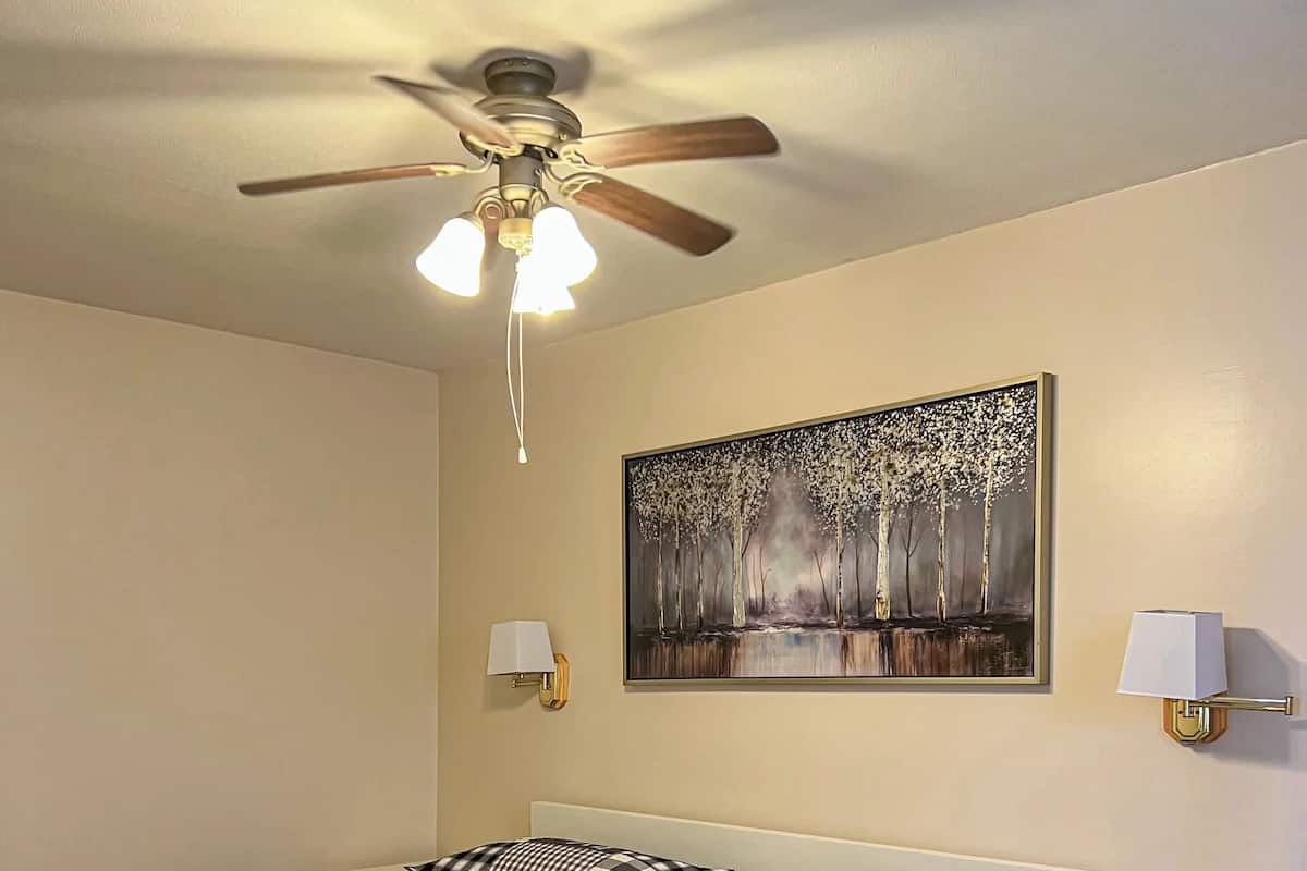 Une chambre à coucher avec un lit, un ventilateur de plafond, une table de chevet, une lampe et un tableau au mur.
