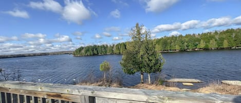 Una terraza de madera con vista a un lago, una isla boscosa y un cielo despejado.