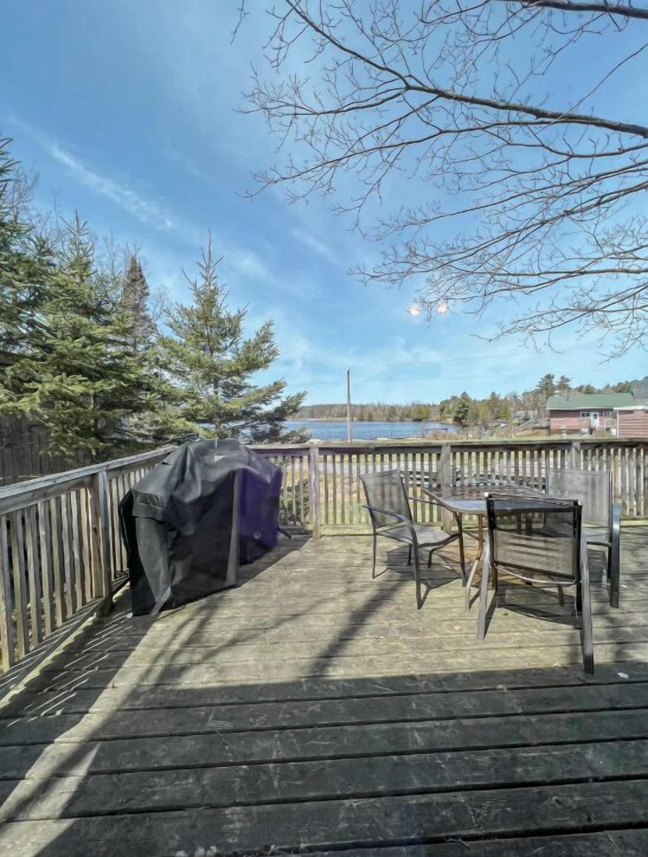 A wooden deck with a table and chairs, overlooking a body of water and trees.