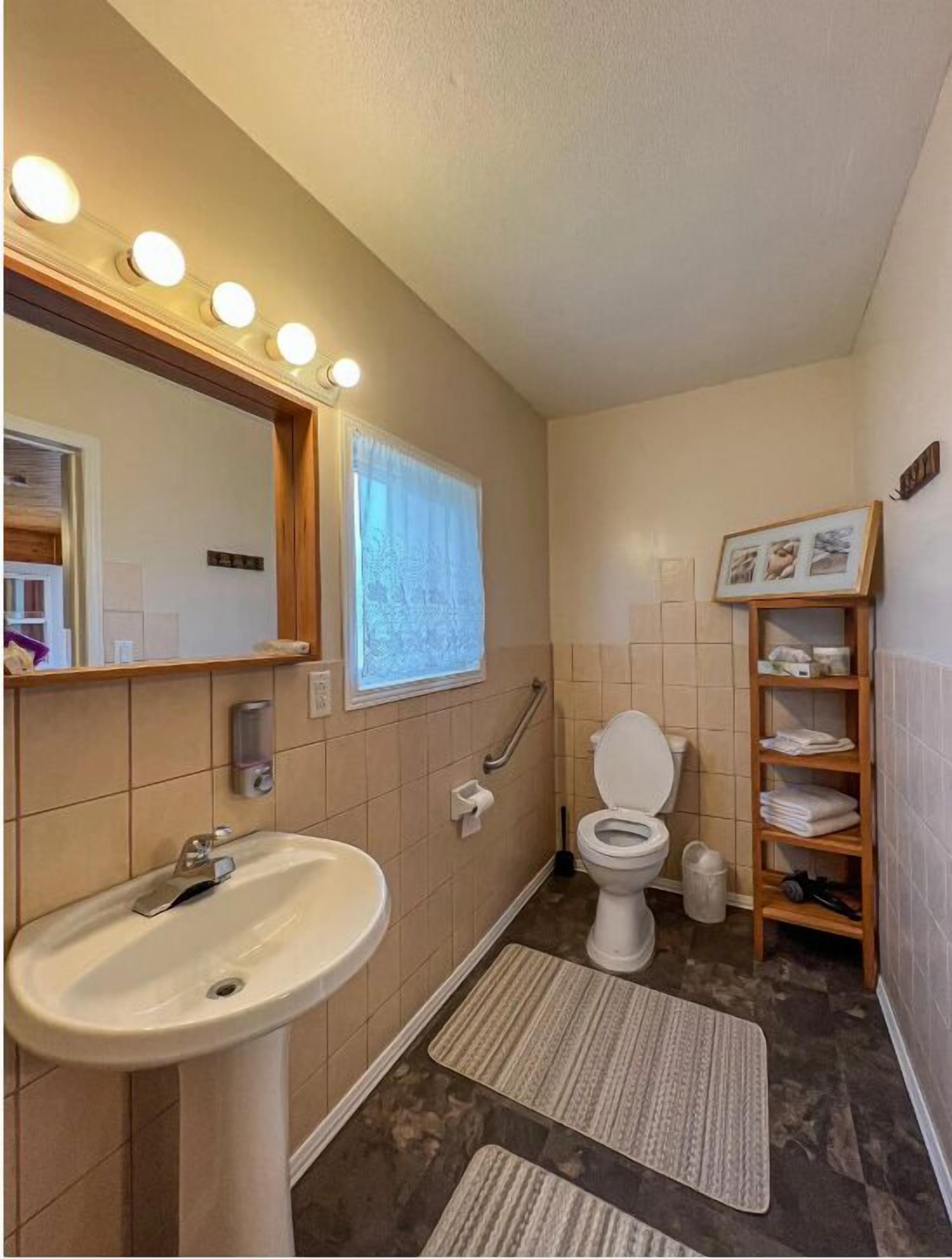 Een badkamer met een wastafel, toilet, spiegelkap en een plank met handdoeken.
