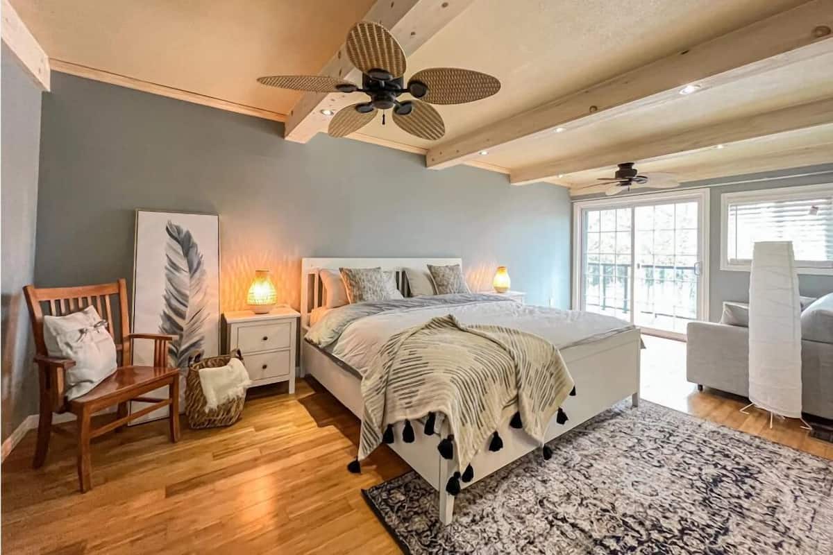 Une chambre à coucher avec un lit, deux lampes de chevet, une chaise en bois, un tapis et un ventilateur de plafond.
