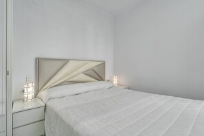 Un lit bien fait, avec une tête de lit, une table de chevet avec une lampe et un luminaire fixé au mur.