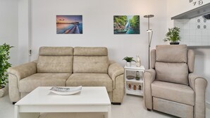 A living room with a beige sofa, a white coffee table, and a recliner. There are two wall-mounted paintings, a floor lamp, and a small shelf with decorative items. - Great Views Studio A84 near the beach with shared pool and Wi-Fi (Torrox)