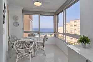 A balcony with a dining table and chairs, large windows with a view of the sea and buildings, and a ceiling fan. - Great Views Studio A84 near the beach with shared pool and Wi-Fi (Torrox)